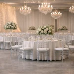 Transparente Chiavari Stühle mit weißen Velvet Sitzpolstern und runden Banketttischen mit bodenlangen Tischdecken kaufen